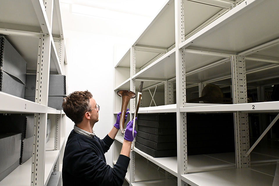 Museum staff member holding a horn in between two white shelving units